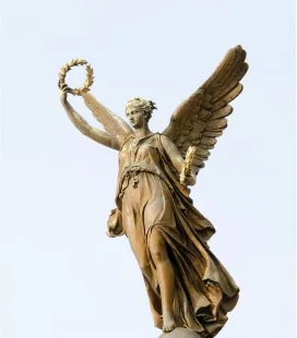 Gold winged statue holding wreath and staff against light blue sky