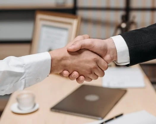 Two professionals shaking hands at a desk in an office setting